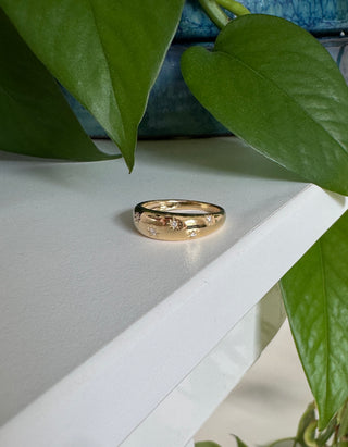 Gold ring on a white surface with green leaves in the background