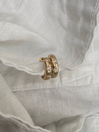 Gold hoop earrings with small diamonds on a white fabric background